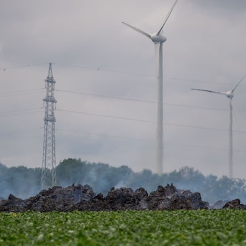 Das Bild zeigt die qualmenden Strohballen. Im Hintergrund dreht sich ein Windrad an der Autobahn.