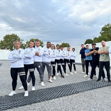Das Bild zeigt die jungen Sportler aus Brühl, die mit verschränkten Armen in einer Reihe posieren. Daneben bilden die Musiker der Gruppe Deichkind eine Reihe.
