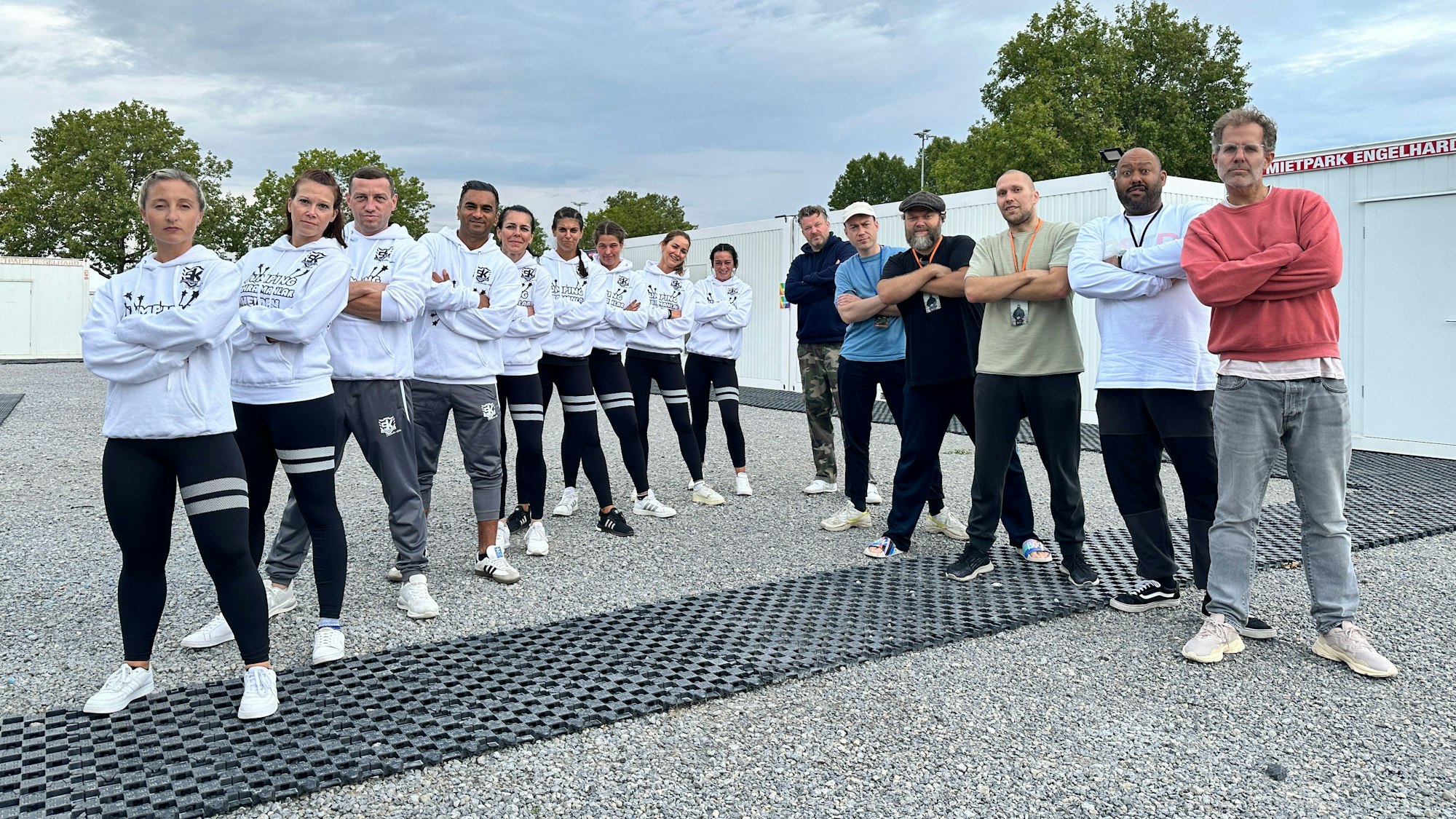 Das Bild zeigt die jungen Sportler aus Brühl, die mit verschränkten Armen in einer Reihe posieren. Daneben bilden die Musiker der Gruppe Deichkind eine Reihe.