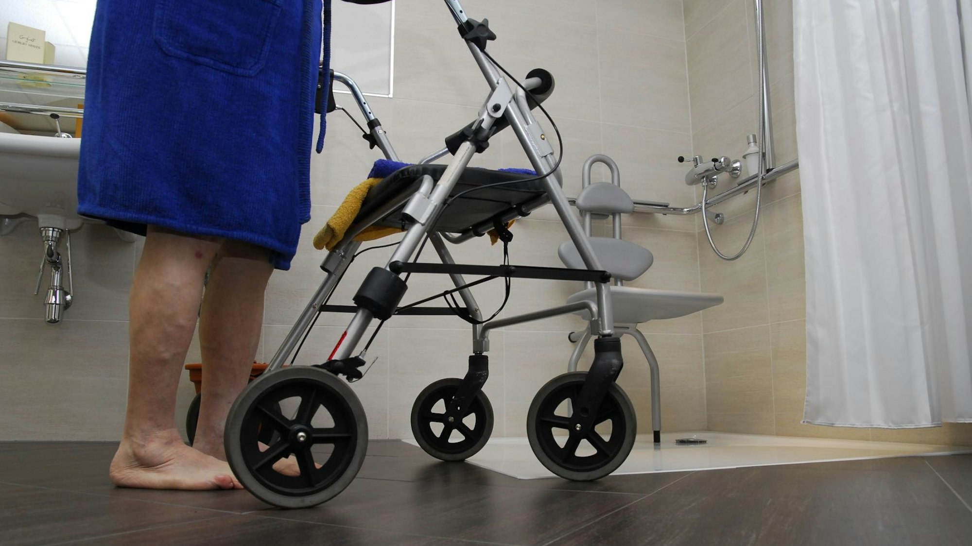 Eine Seniorin geht mit ihrem Rollator in eine bodengleiche Dusche.