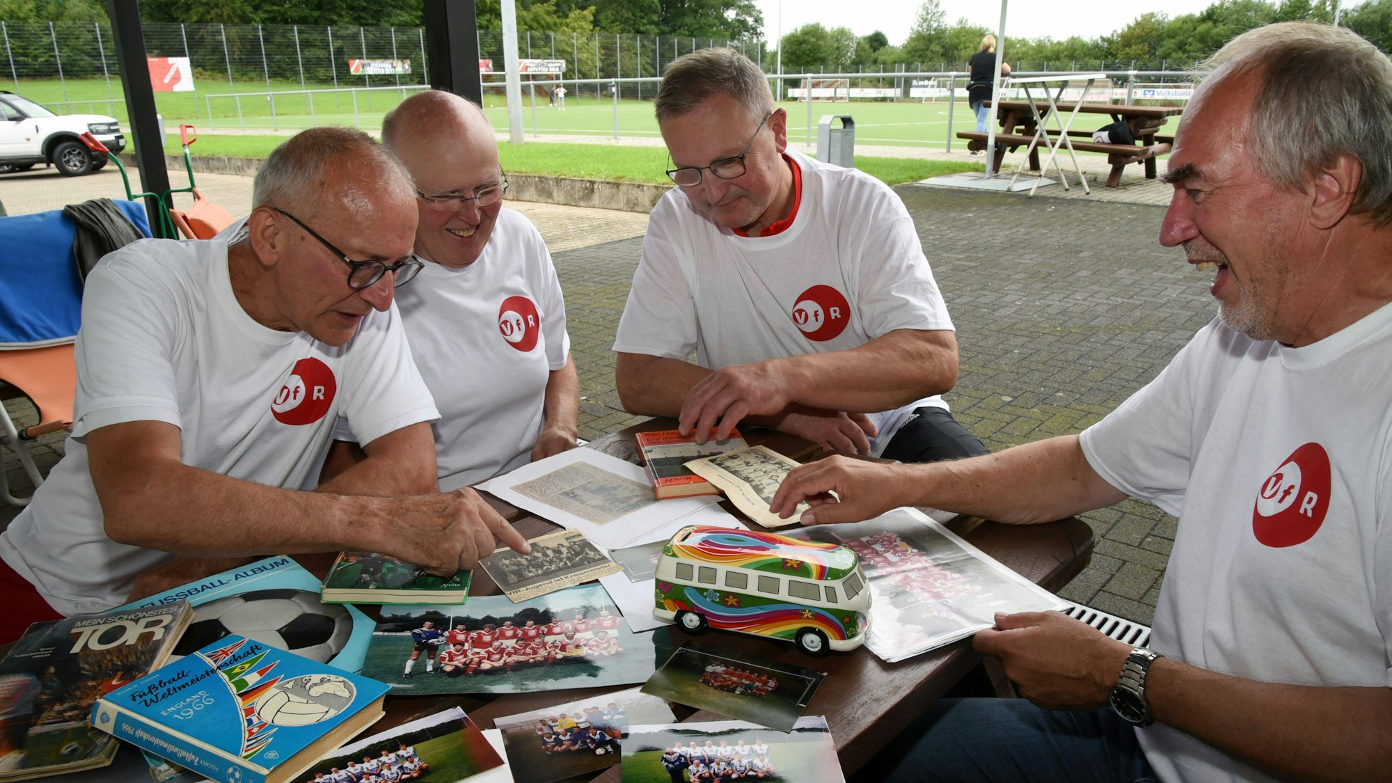 Vier Männer schauen sich alte Fotos und Zeitungsartikel an.