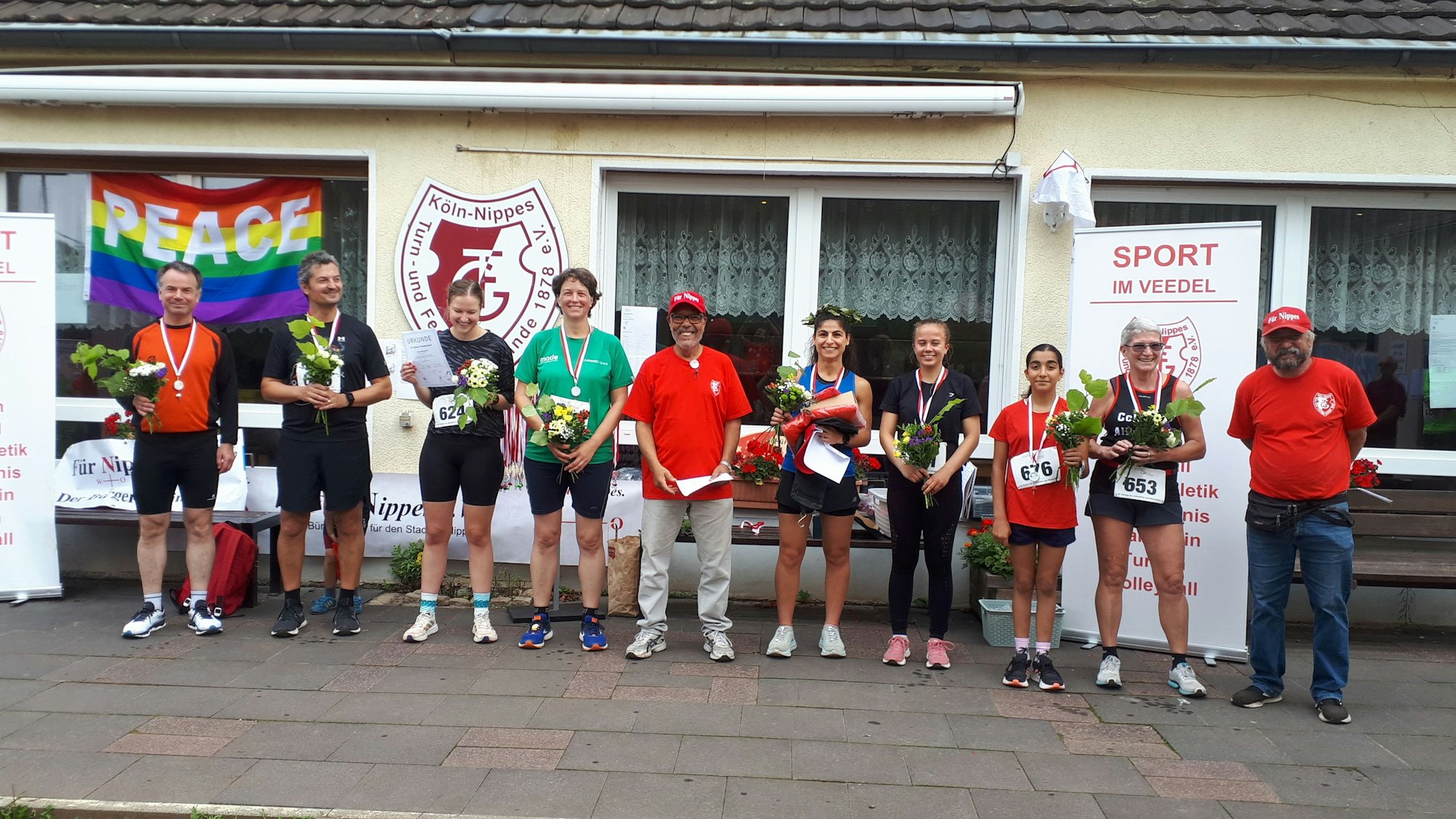 Männer und Frauen stehen mit Medaillen um den Hals vor einem Vereinsheim.