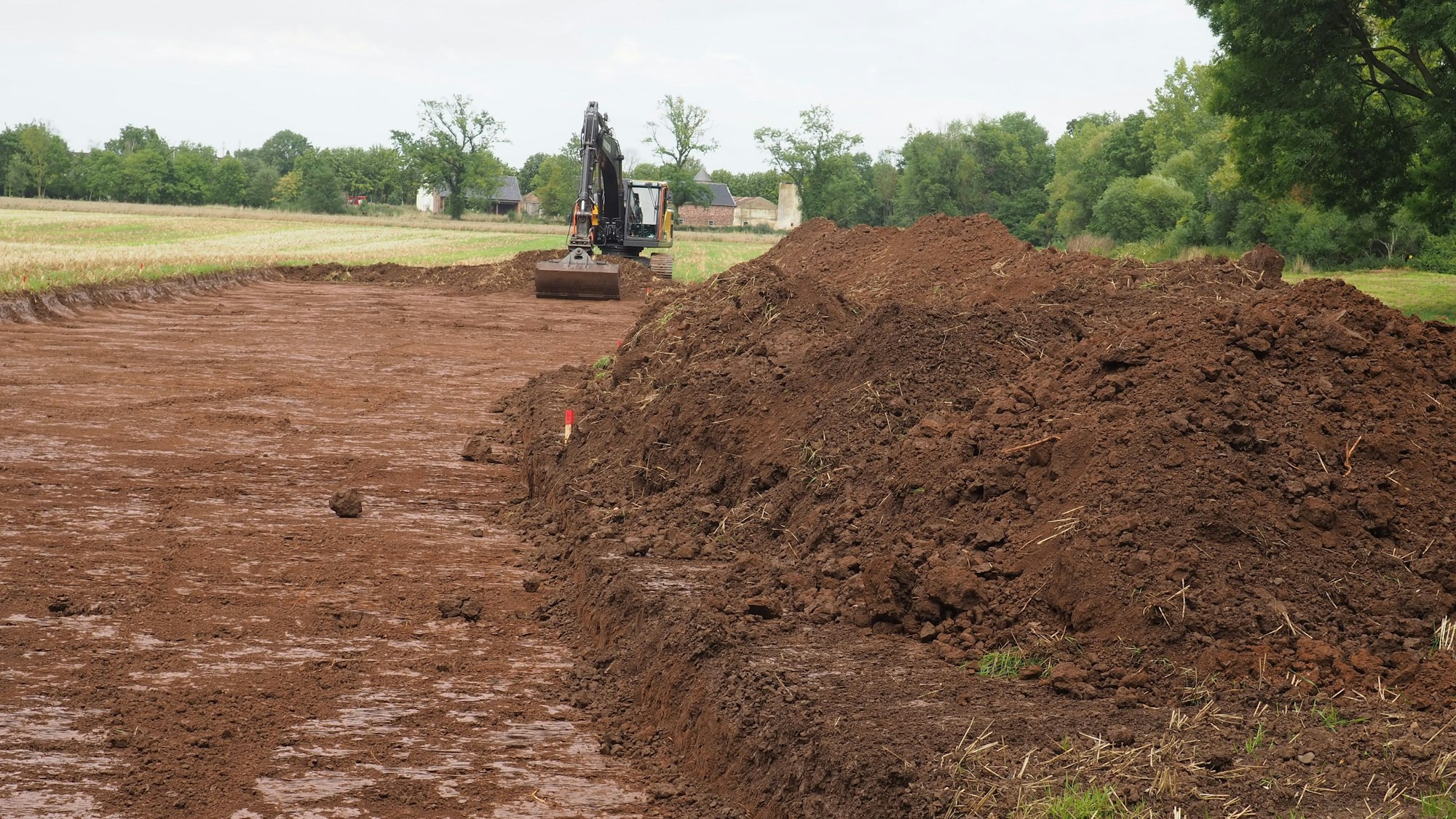 Ein Bagger hat Erde auf einem Feld abgetragen und zu einem Wall aufgehäuft.
