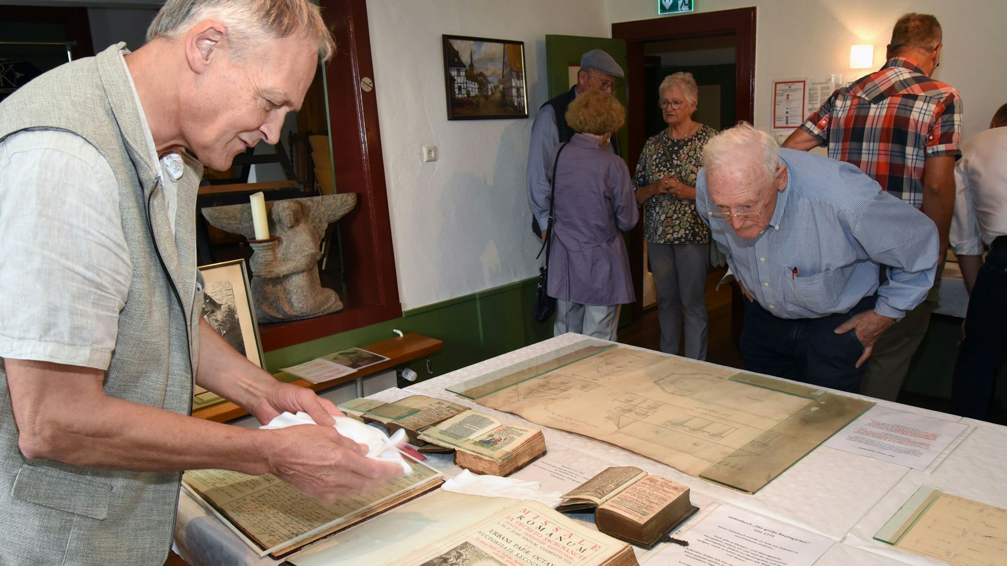 Zwei ältere Männer schauen sich in einer Ausstellung Reliquien an, die auf einem Tisch liegen.