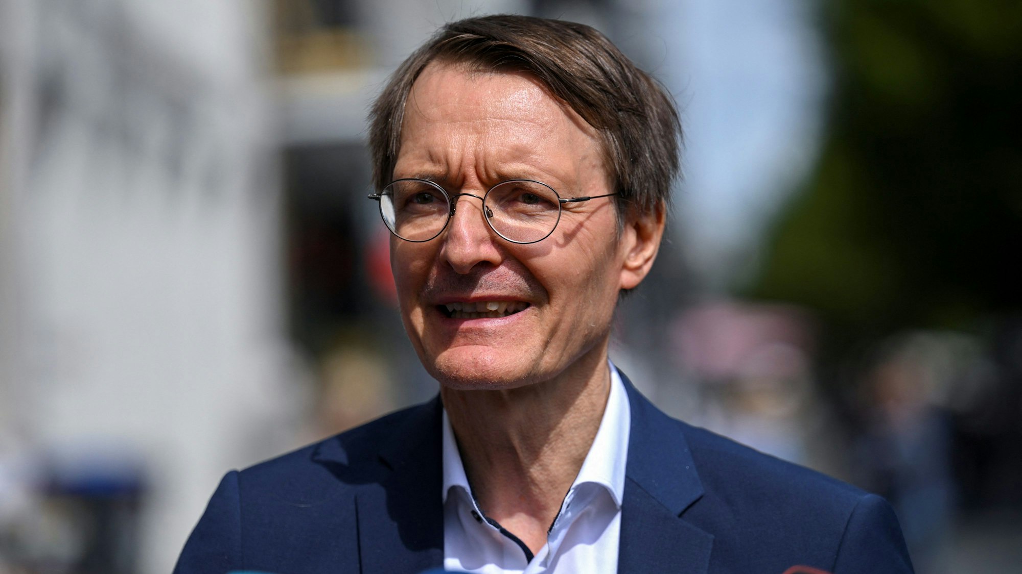 Bundesgesundheitsminister Karl Lauterbach (SPD) steht bei einer Pressekonferenz im Anzug vor mehreren Mikrofonen von Fernsehsender.