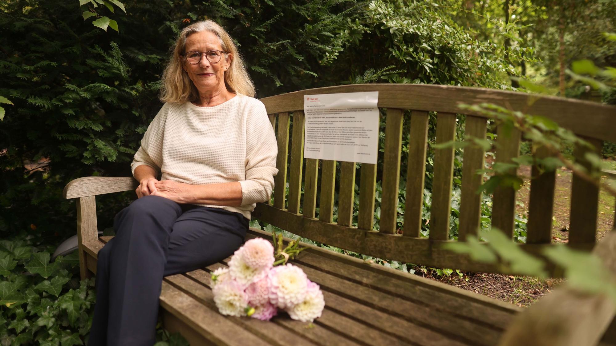 Eine Frau sitzt auf einer Holzbank auf dem Friedhof.