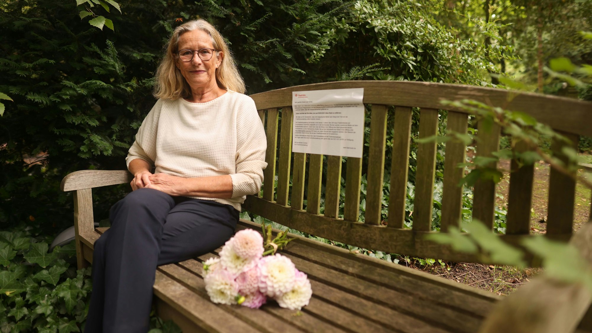 Eine Frau sitzt auf einer Holzbank auf dem Friedhof.