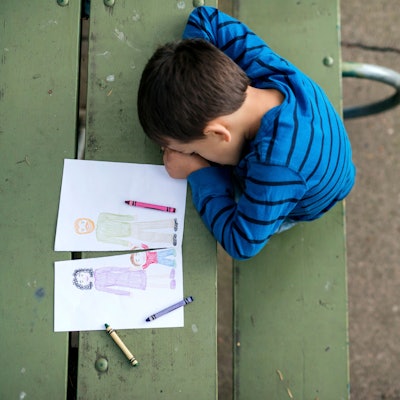 Trauriger Junge hat den Kopf auf einen Tisch gelegt, neben ihm die zerschnittene Zeichnung einer Familie
Getty Images FatCamera