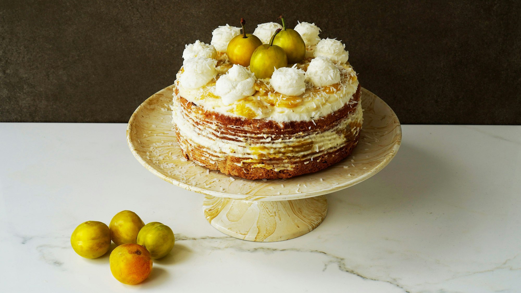 Eine Mirabellentorte steht auf einem Kuchenteller. Frische Mirabellen liegen auf dem Kuchen und neben dem Teller.
