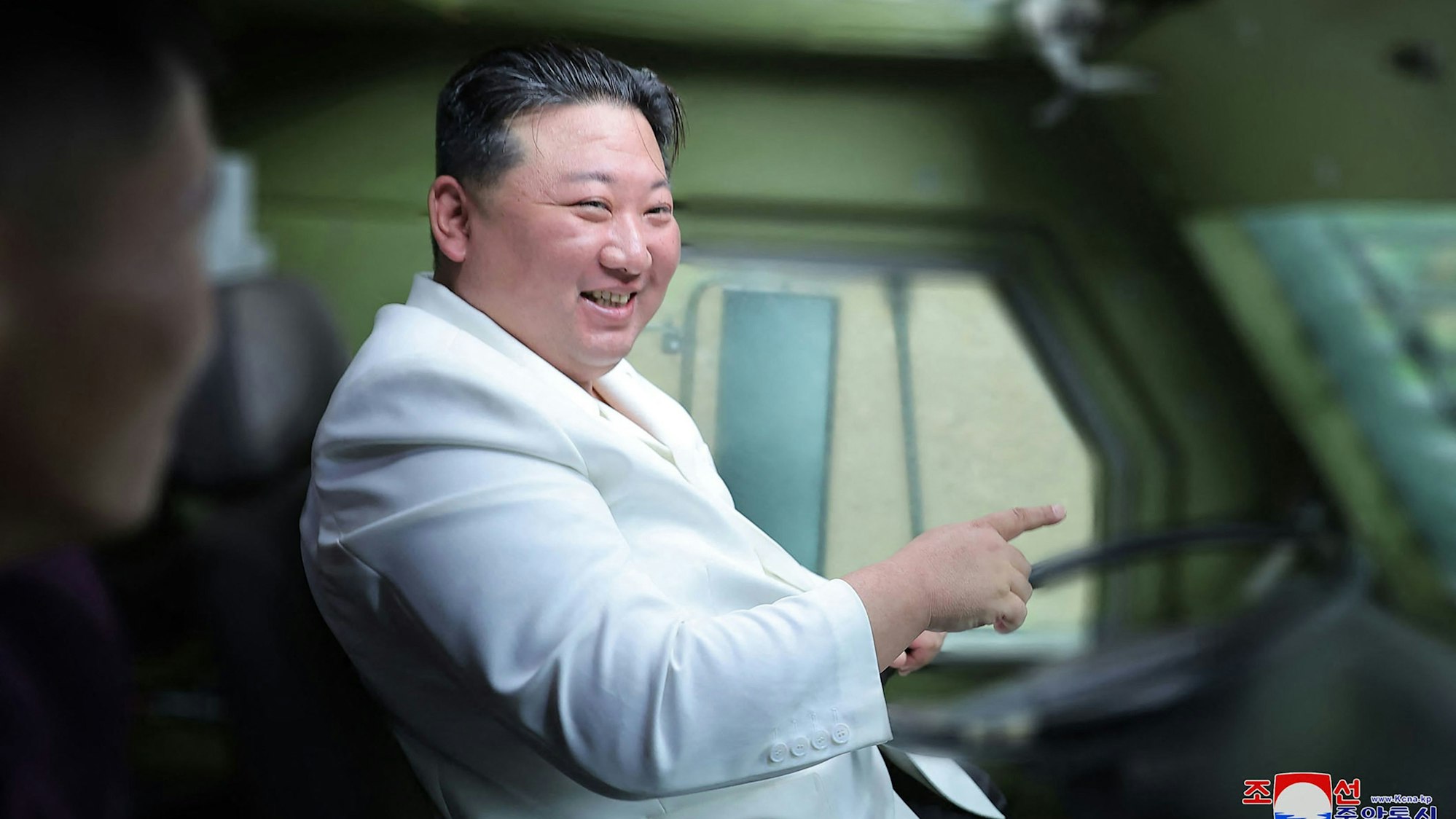 Kim Jong Un sitzt lachend in einem Militärfahrzeug am Steuer.