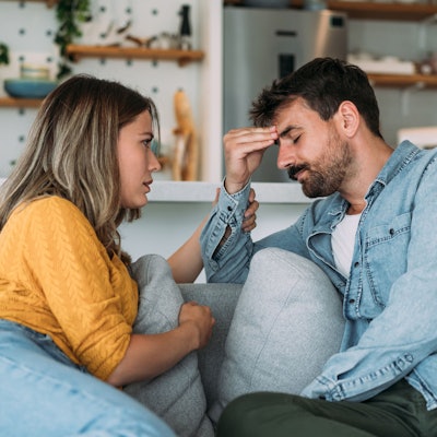 Ein junges Paar bespricht auf dem Sofa ein Problem, der Mann wirkt sehr frustriert