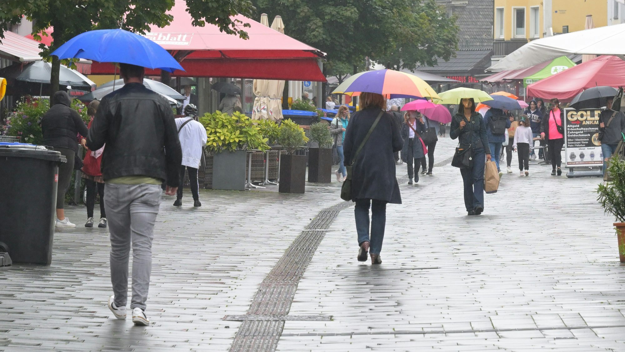 Menschen gehen mit Schirmen durch die Bergisch Gladbacher Fußgängerzone.