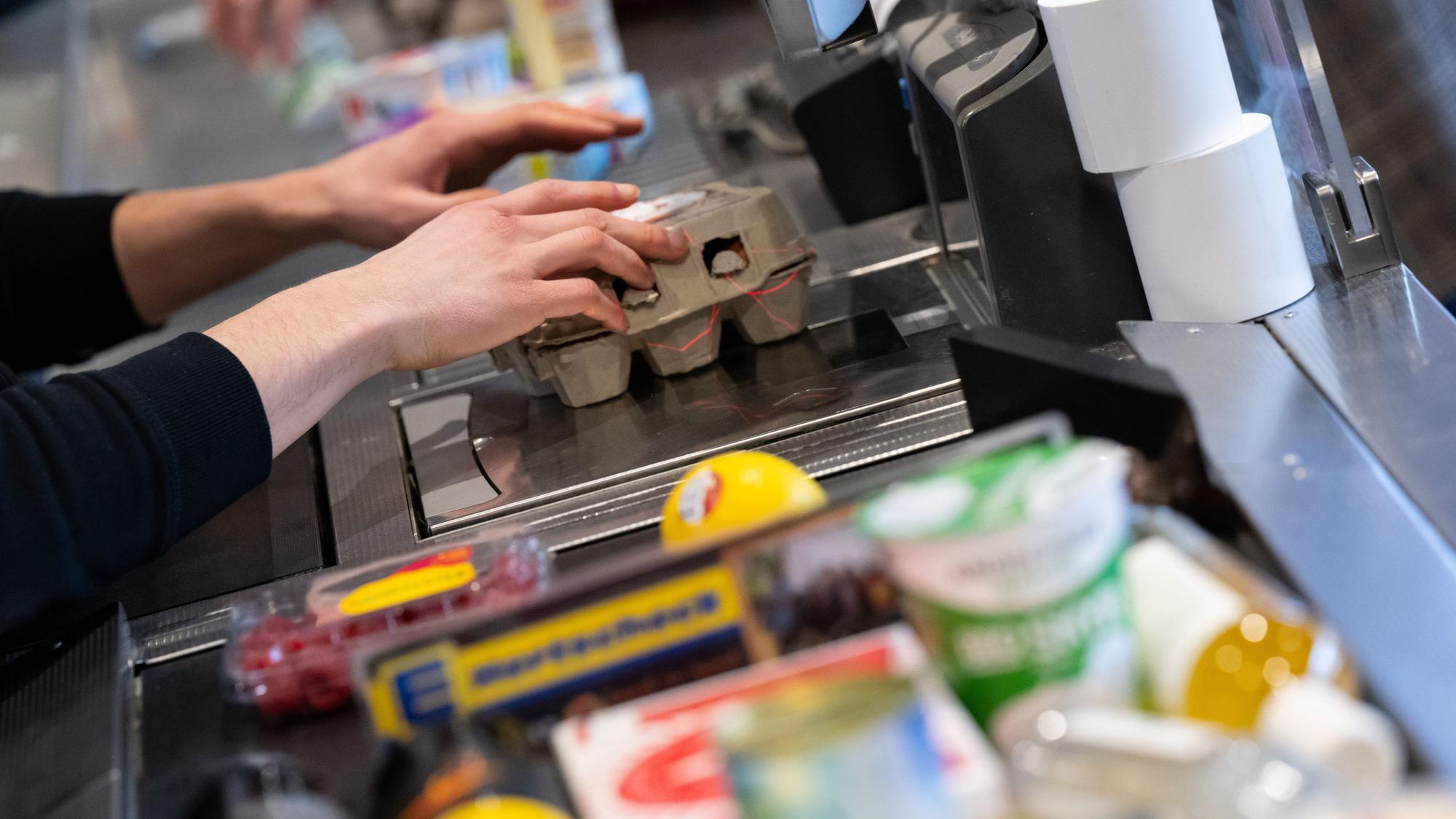 An einer Supermarktkasse zieht ein Kassierer Ware über den Scanner.