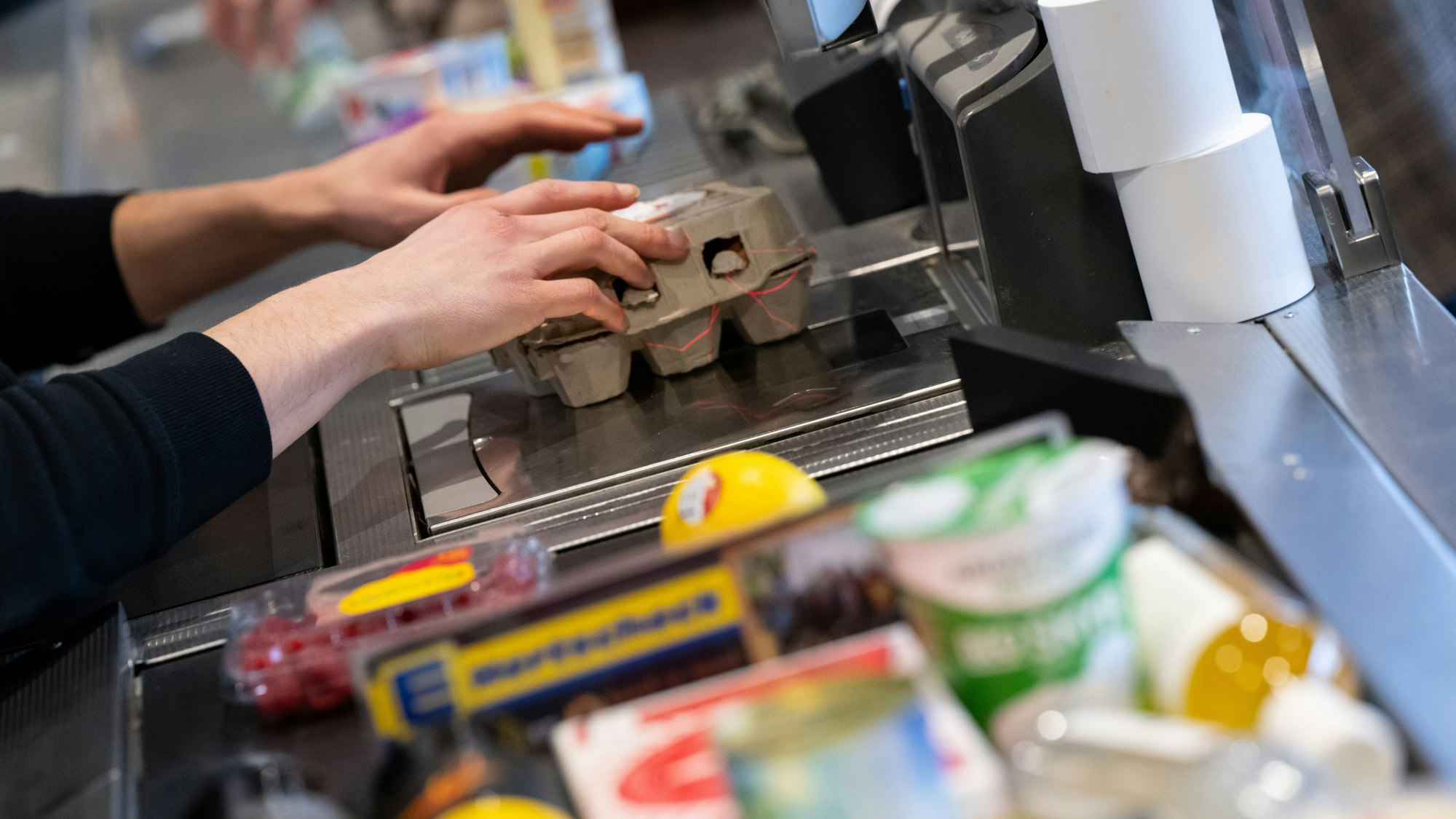 An einer Supermarktkasse zieht ein Kassierer Ware über den Scanner.