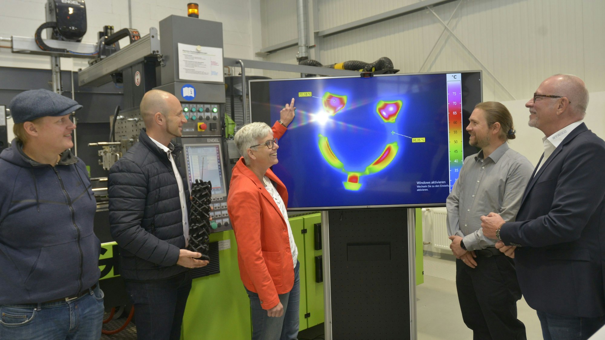 An einem Bildschirm, auf dem Temperaturunterschiede farblich angezeigt werden, stehen mehrere Männer und eine Frau, die mit dem Finger auf den Bildschirm zeigt.