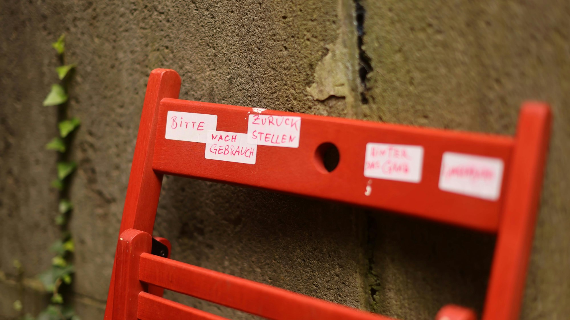 Ein Stuhl lehnt hinter einem Grabstein, der Besitzer bittet darum, ihn zurückzustellen, wenn man ihn ausleihen möchte.