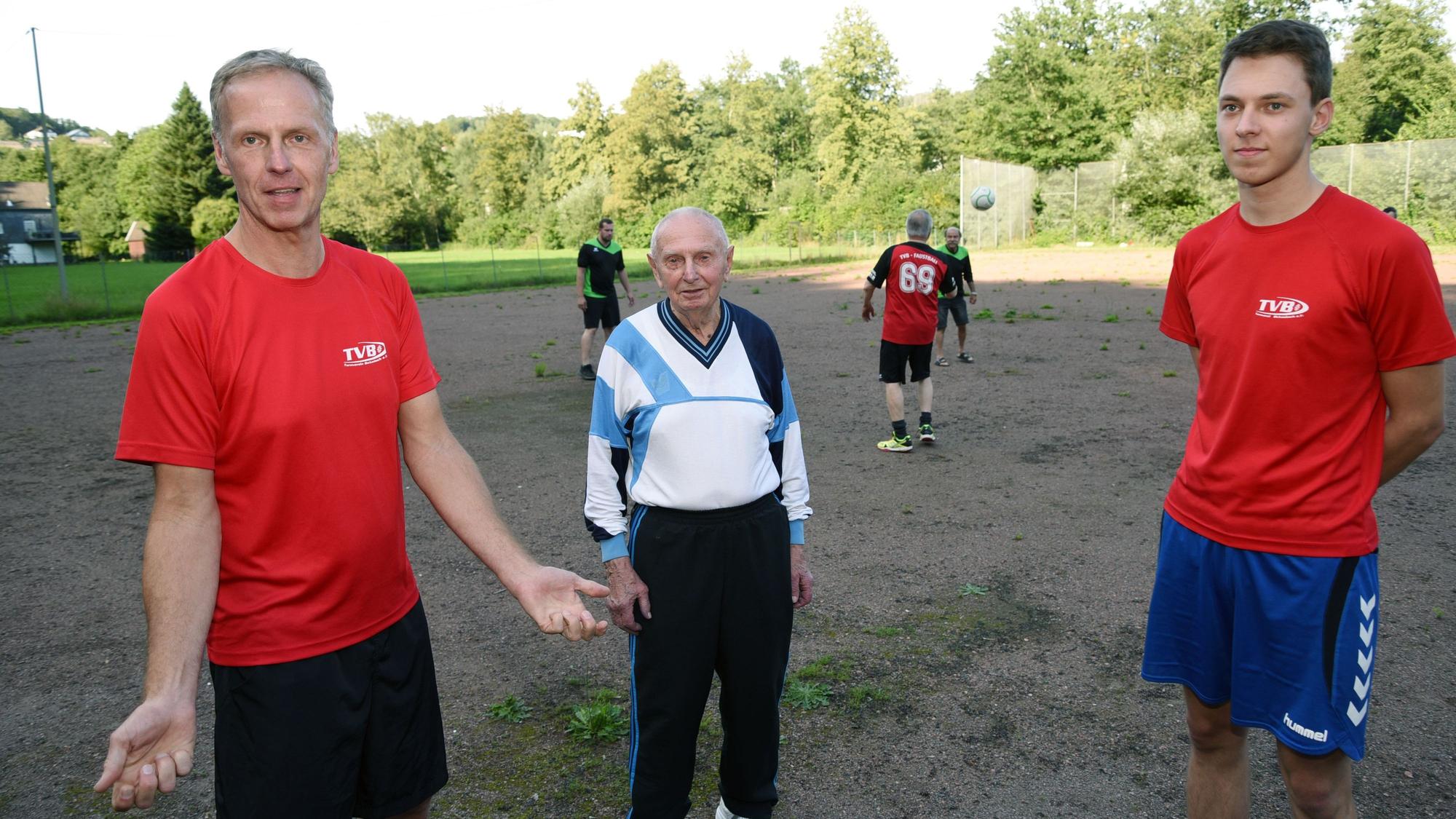 Drei Männer aus drei Familiengenerationen stehen auf einem Sportplatz nebeneinander: Vater, Sohn und Enkel.