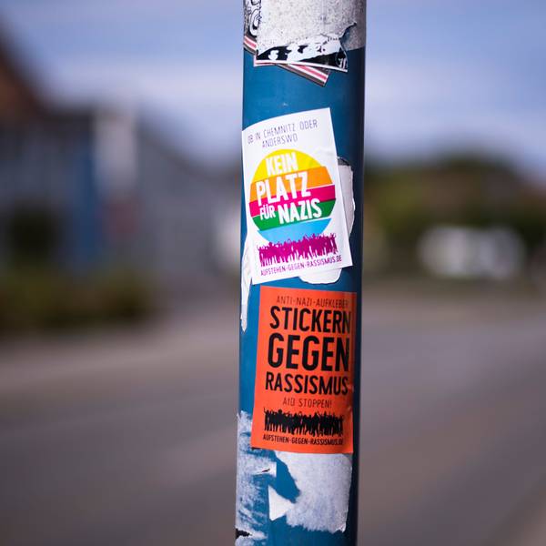 Auf einer Straßenlaterne sind Sticker gegen Nazis und Rassismus aufgeklebt.