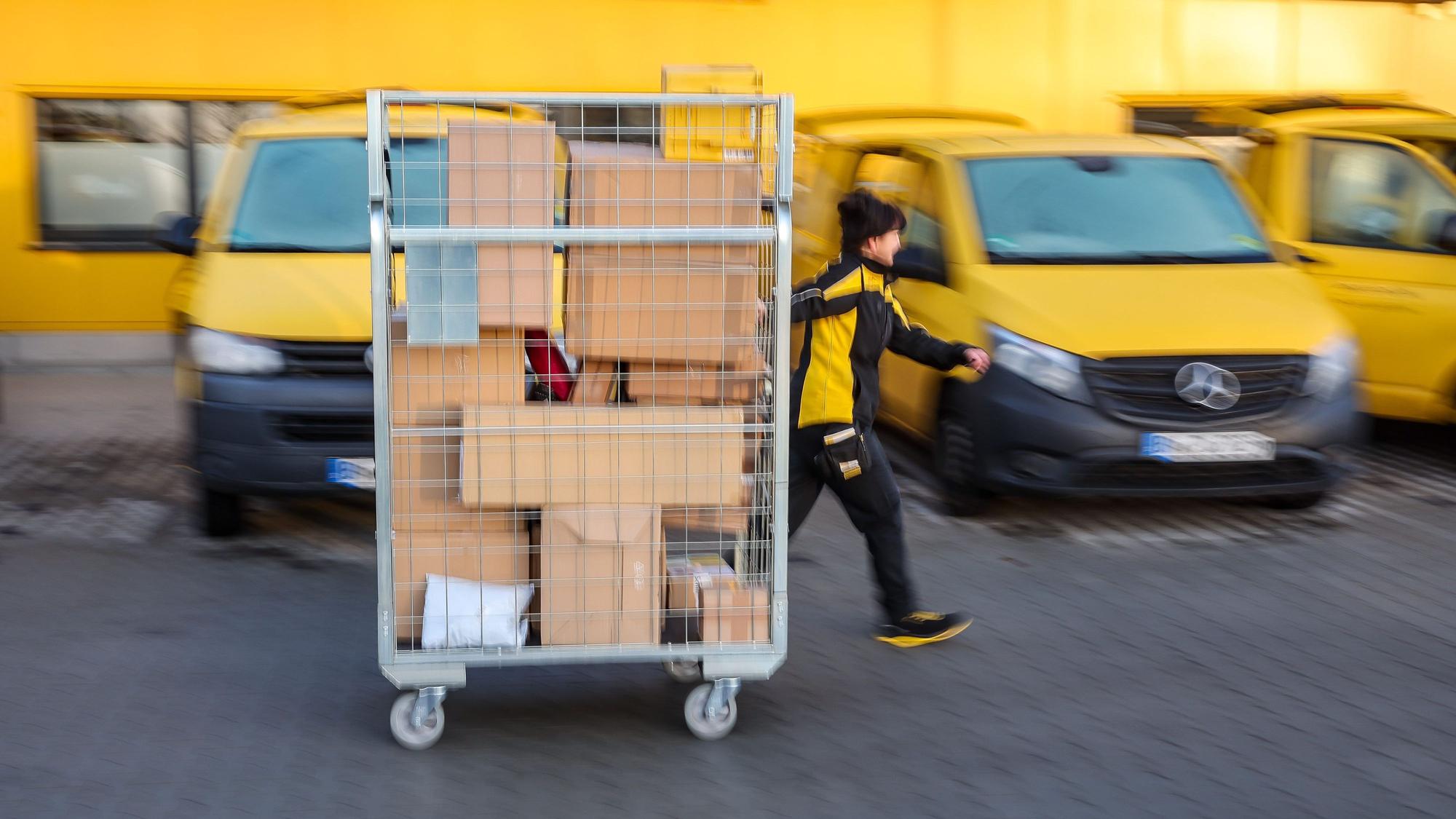 Eine Mitarbeiterin der Deutsche Post DHL geht mit einem vollen Paketwagen zu ihrem Fahrzeug auf dem Hof eines Zustellpunktes.