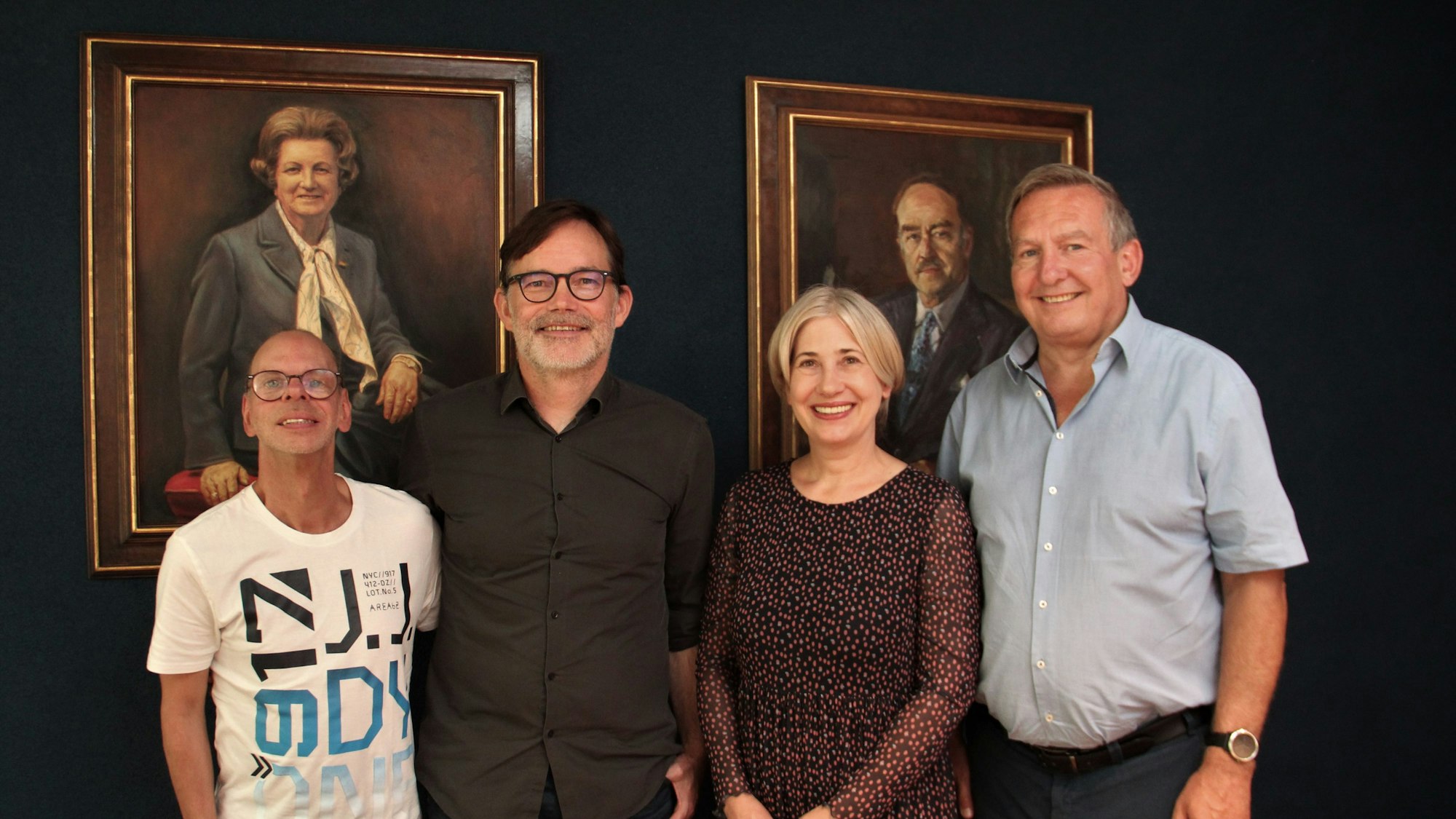 Vier Menschen stehen vor zwei Gemälden in einer Reihe.