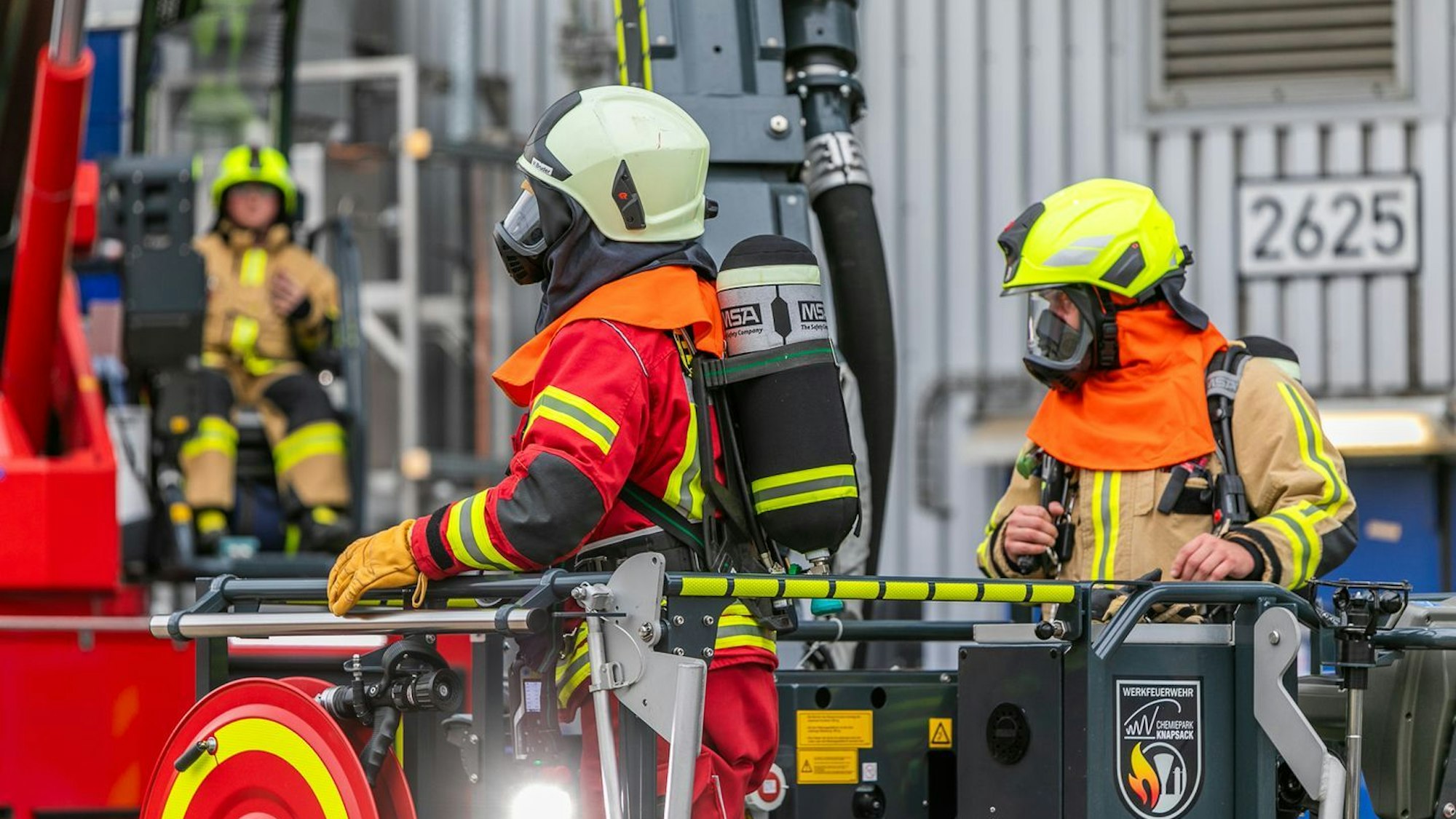 Feuerwehrleute mit Helm und Maske an einem Einsatzfahrzeug.