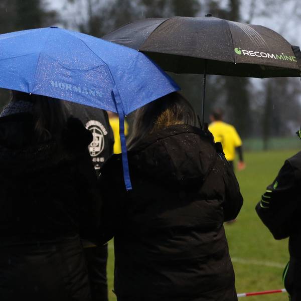 Zwei Zuschauerinnen stehen mit Regenschirm am Rande eines Fußballspiels.