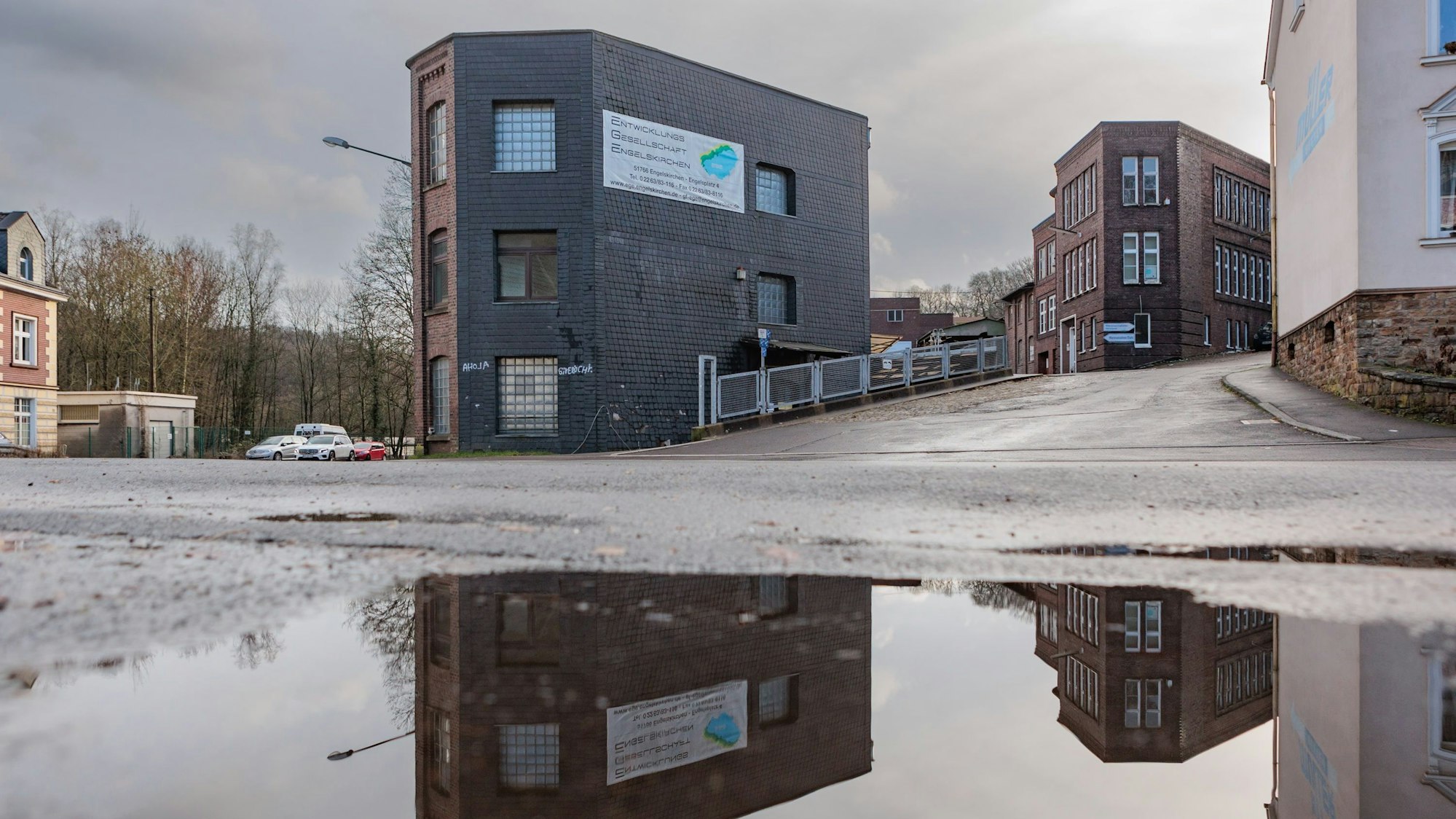 Die alten Gebäude der Bücherfabrik spiegeln sich in einer Pfütze.