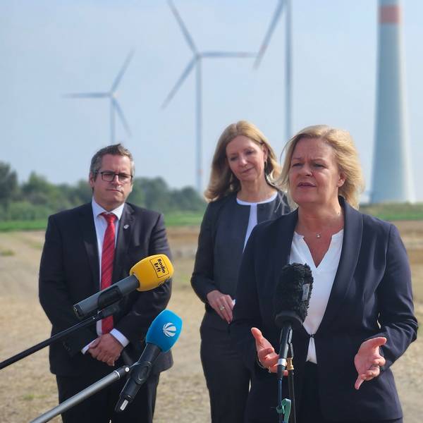Bundesinnenministerin Nancy Faeser spricht vor Windrädern bei einem Pressetermin in Mikrophone. Hinter ihr stehen Bedburgs Bürgermeister Sascha Solbach und zwei Frauen von RWE.