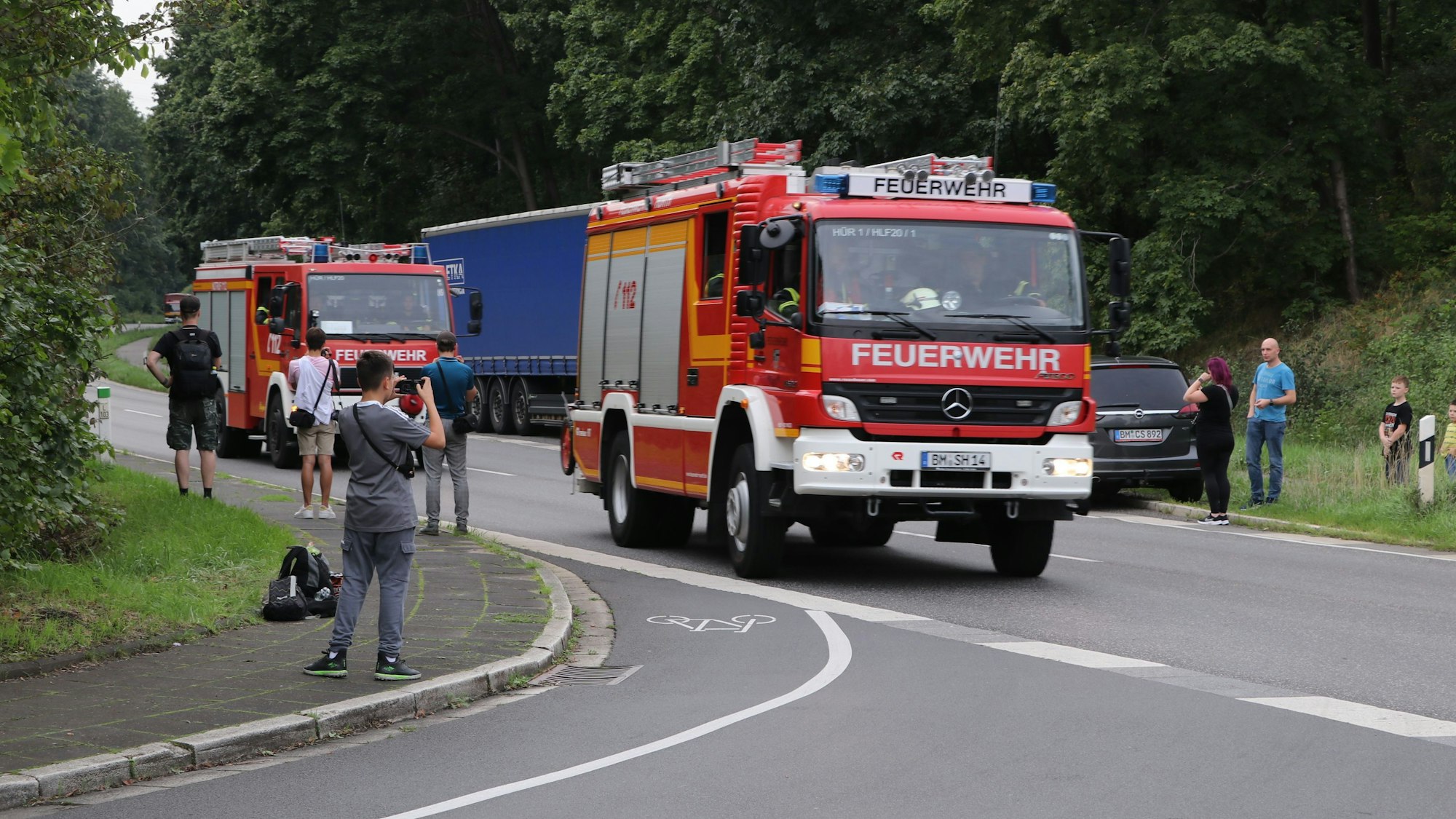 Jugendliche fotografieren vom Straßenrand aus Feuerwehrwagen.