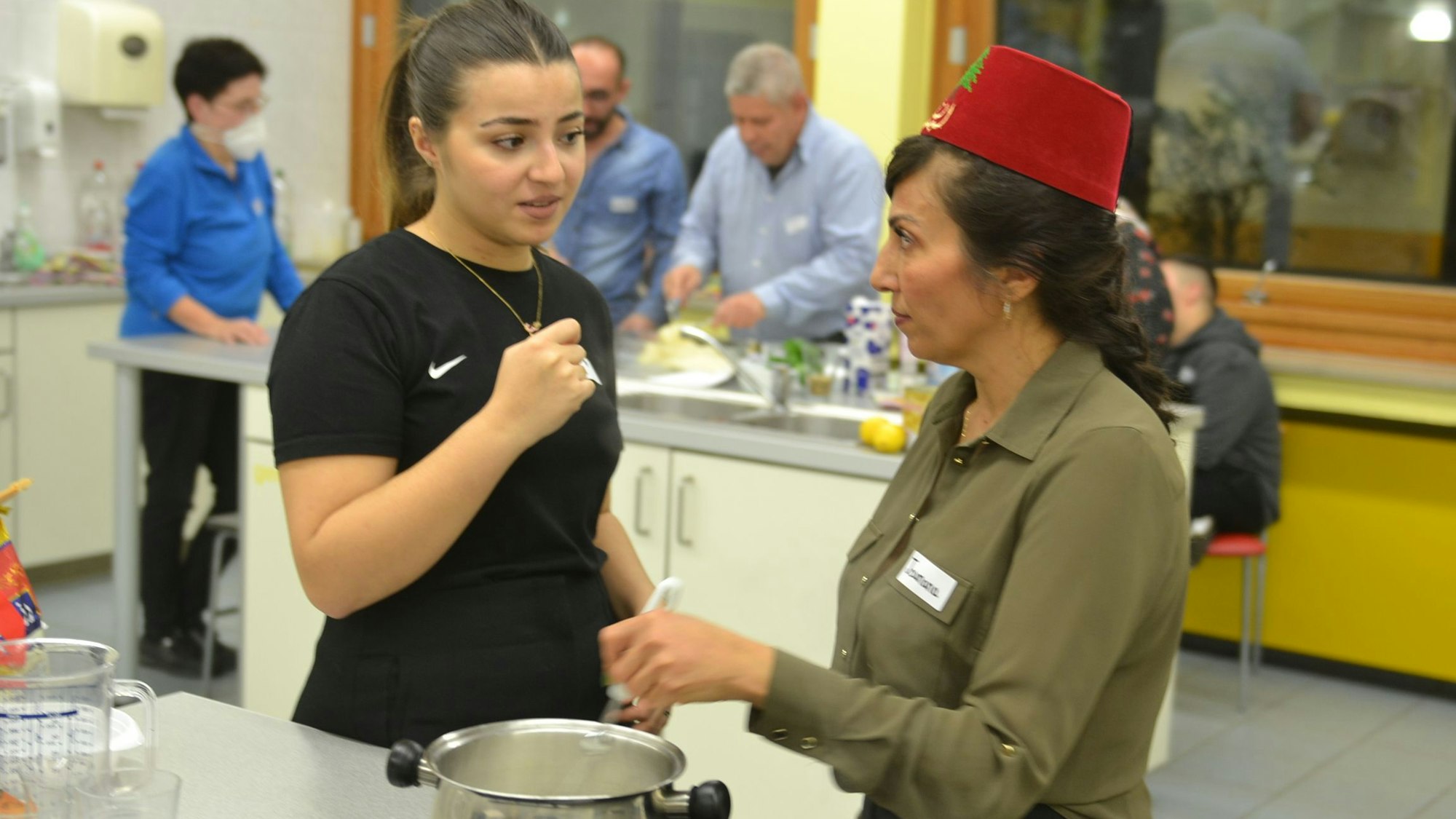 Das Bild zeigt zwei Frauen, die in der Küche stehen und kochen.
