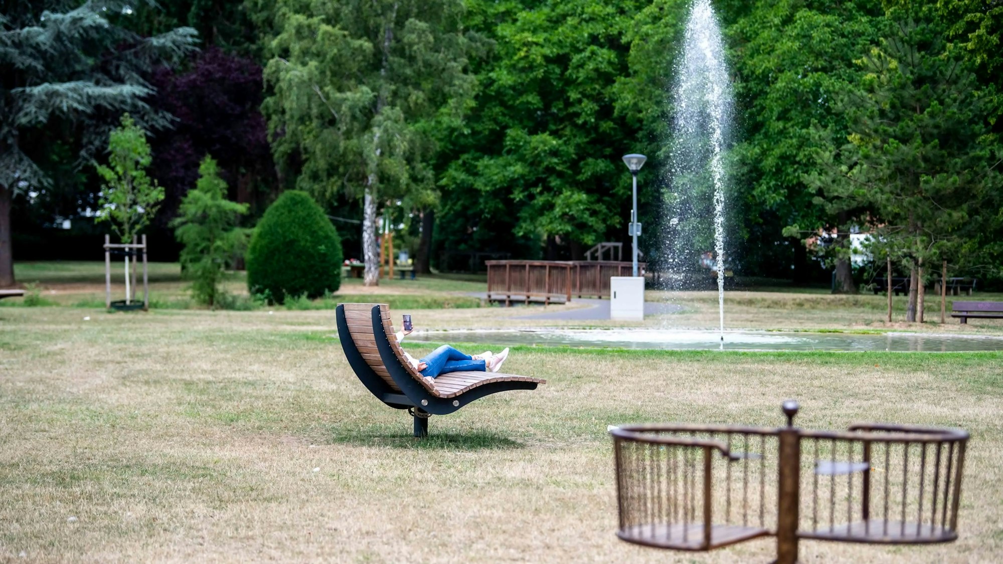 Das Bild zeigt den Ruhrpark. Auf einer großen Holzliege sitzt eine Frau.