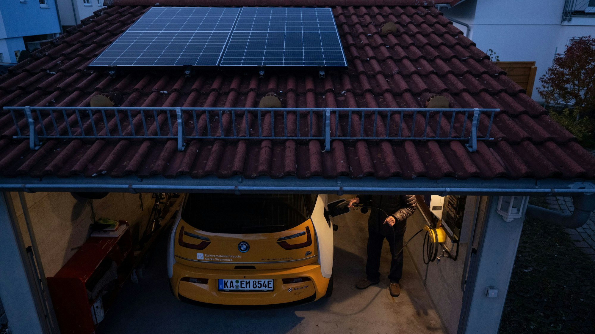 Eine geöffnete Garage mit E-Auto und Wallbox und Solar auf dem Dach in der Dämmerung