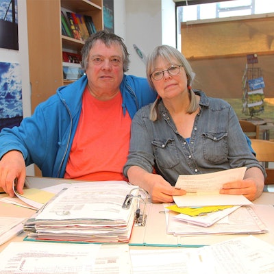 Hartwig Kausch und Silvia Kock sitzen an einem Tisch. Vor ihnen liegen Aktenordner und Papierstapel.