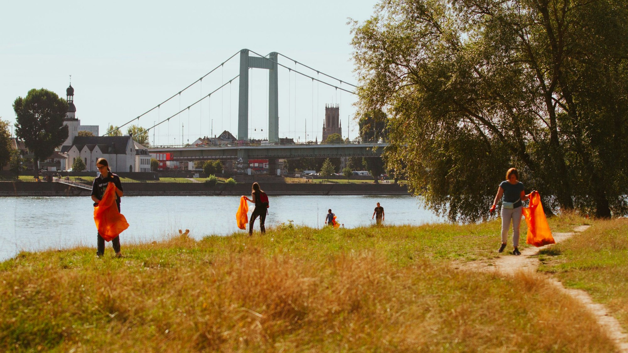 Menschen mit Mülltüten sammeln Unrat am Rheinufer in Niehl.