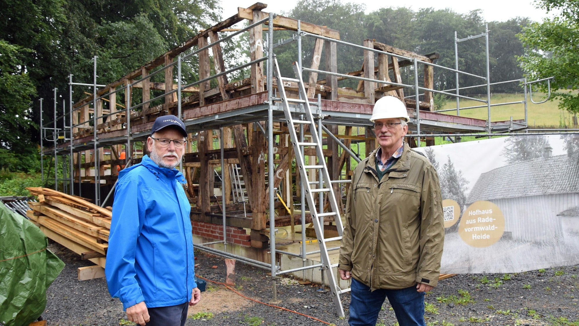Werner Hütt und Burkhard Zinn stehen vor dem Gerüst des Fachwerkhauses, das derzeit wieder aufgebaut wird.