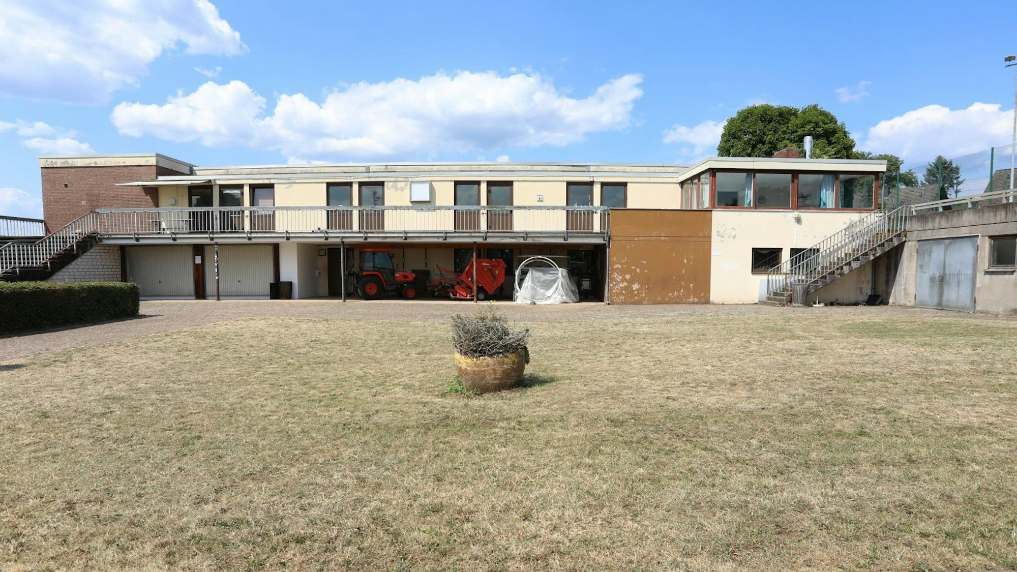 Die Rückseite der Sporthalle Menzenberg mit in die Jahre gekommenen Bauten. Im Vordergrund steht ein Blumenkübel.