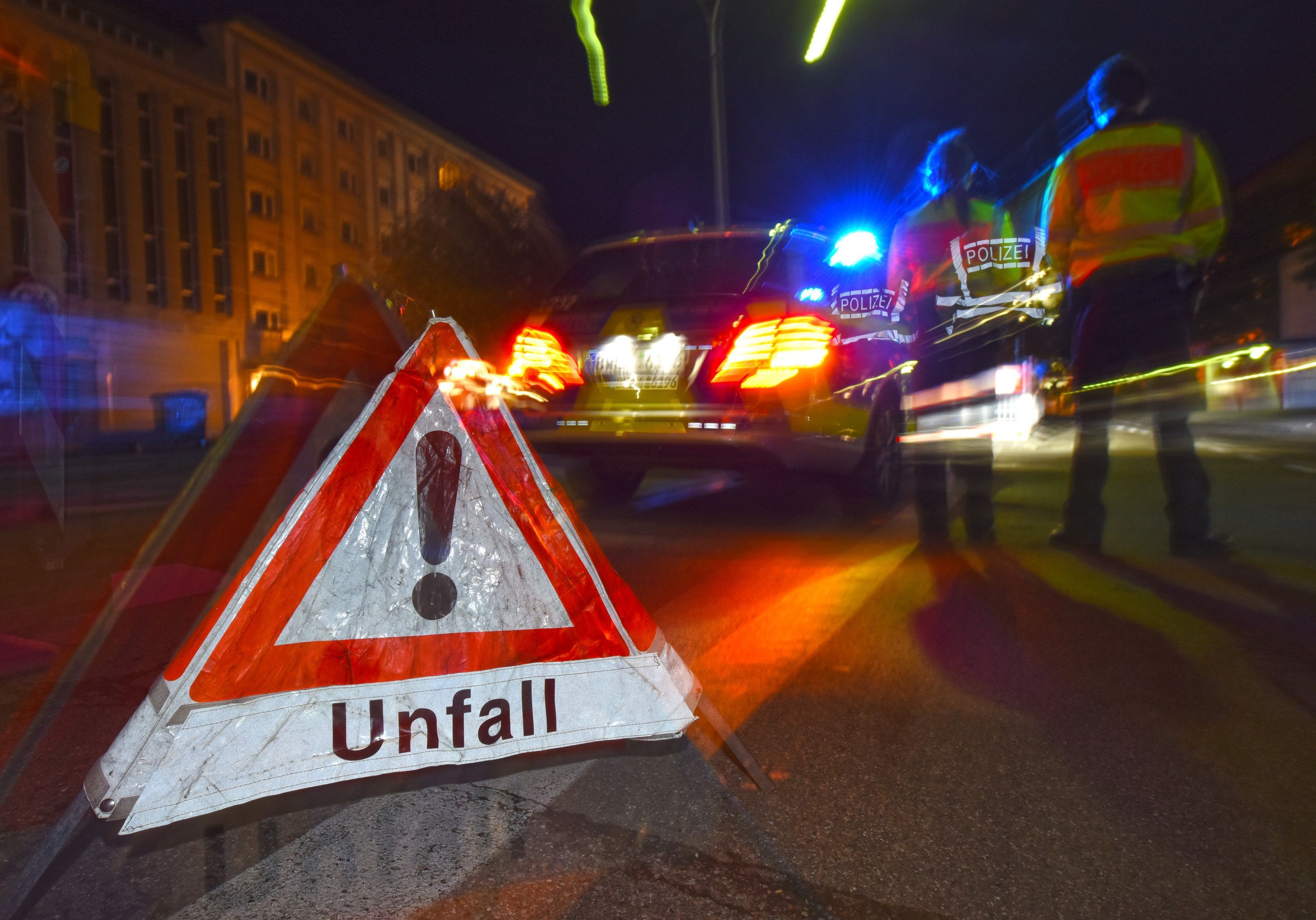 Ein Polizeifahrzeug steht mit Blaulicht auf der Straße. Daneben steht ein Warndreieck mit dem Schriftzug «Unfall».
