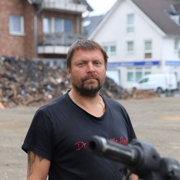 Ein bärtiger Mann im schwarzen T-Shirt steht vor einem großen Schutthaufen.