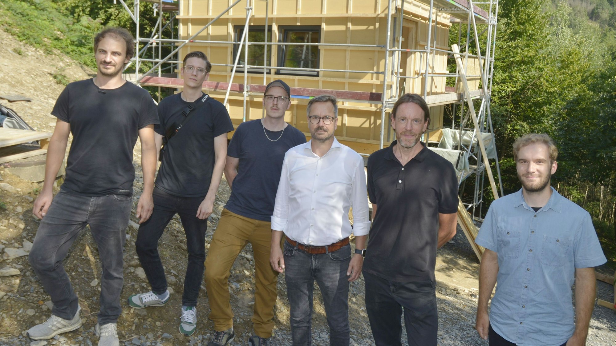 Sechs Männer stehen vor einem Häuserneubau.