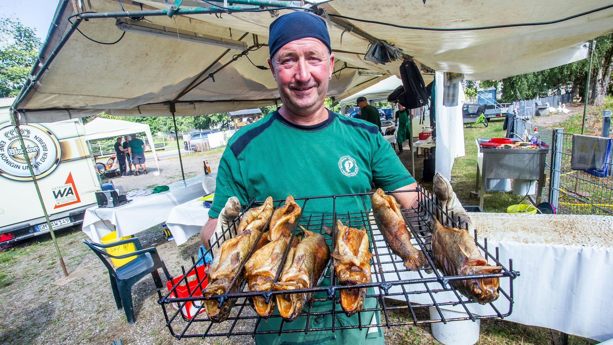 Ein Mann hält ein Grillrost in den Händen. Darauf liegen mehrere geräucherte Fische.