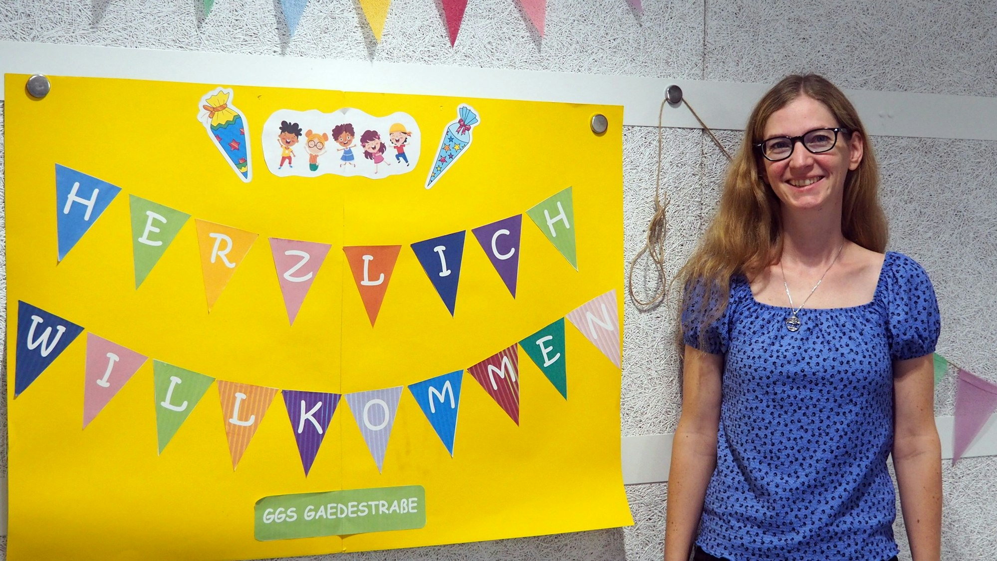 Die Schulleiterin steht neben einem Schulplakat.