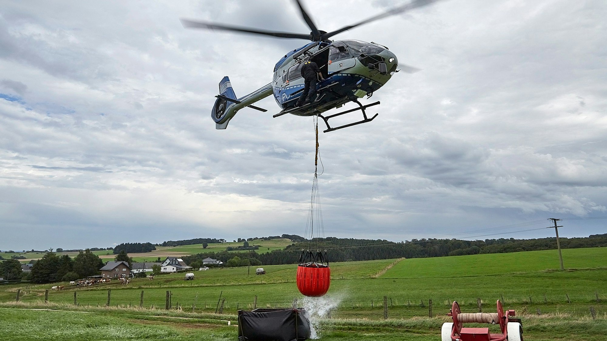 Das Bild zeigt den Polizeihubschrauber mit dem angehängten Wasserbehälter, der gerade aus einem Faltbehälter befüllt worden ist.