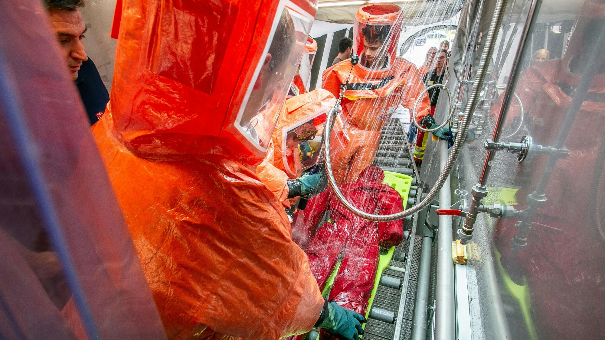 Notfallsanitäter-Azubis in Schutzanzügen proben in einem Zelt den Ernstfall eines ABC-Alarms und die Arbeit in einer Dekontaminationsstraße.