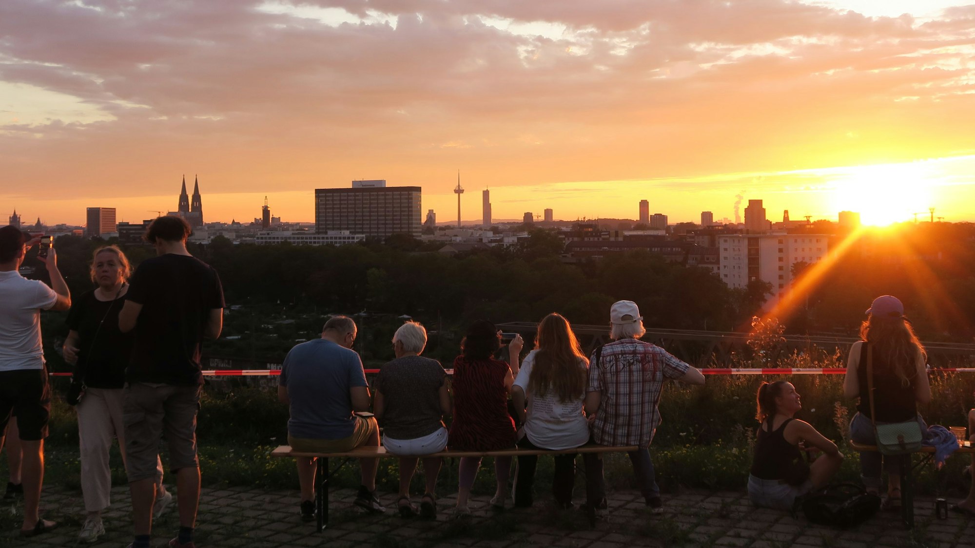 Menschen sitzen im Sonnenuntergang vor dem Panorama Kölns.