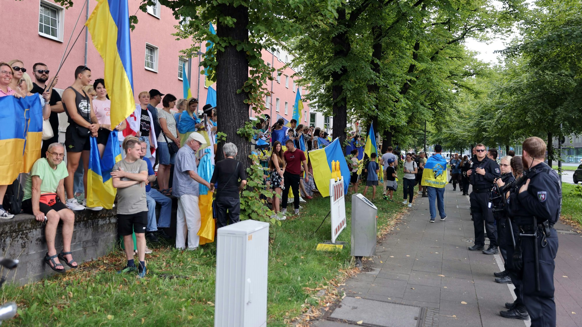 Gegendemonstrationen mit Fahnen stehen in einer Reihe vor der Polizei an der Straße