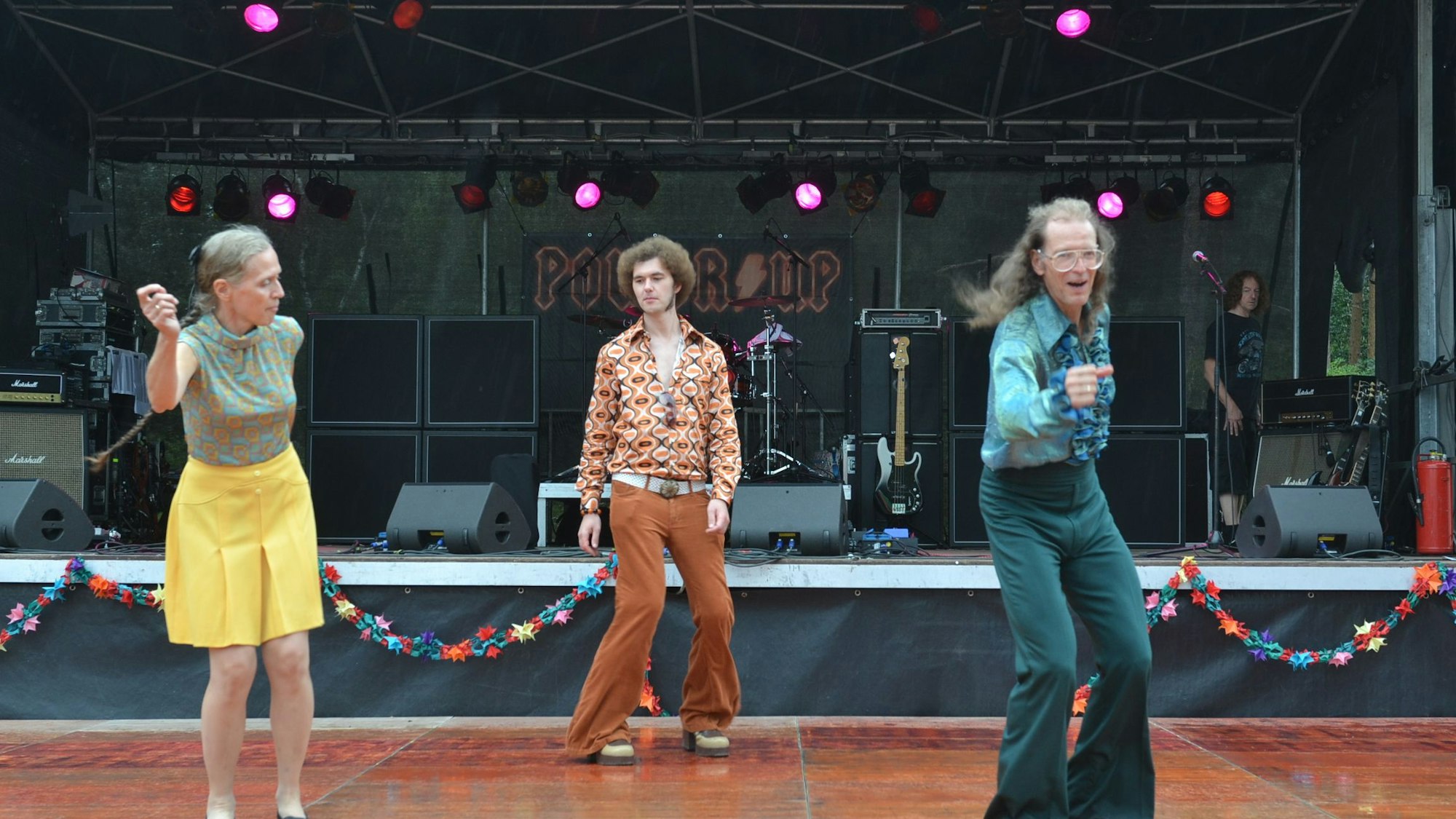 Das Bild zeigt drei Tänzer der Holly Hoppers. Sie tragen gemusterte Hemden und Schlaghosen.