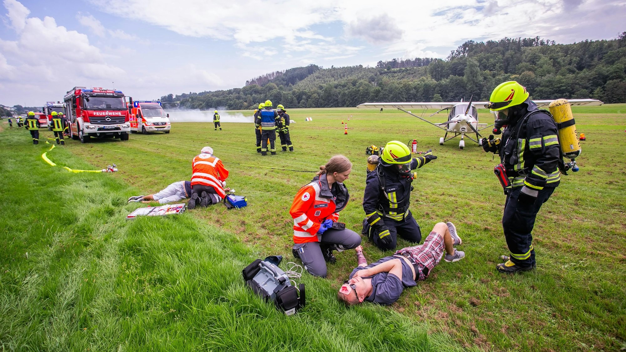 Feuerwehrleute und Rettungssanitäter versorgen einen Verletzten auf einem Flugplatz.
