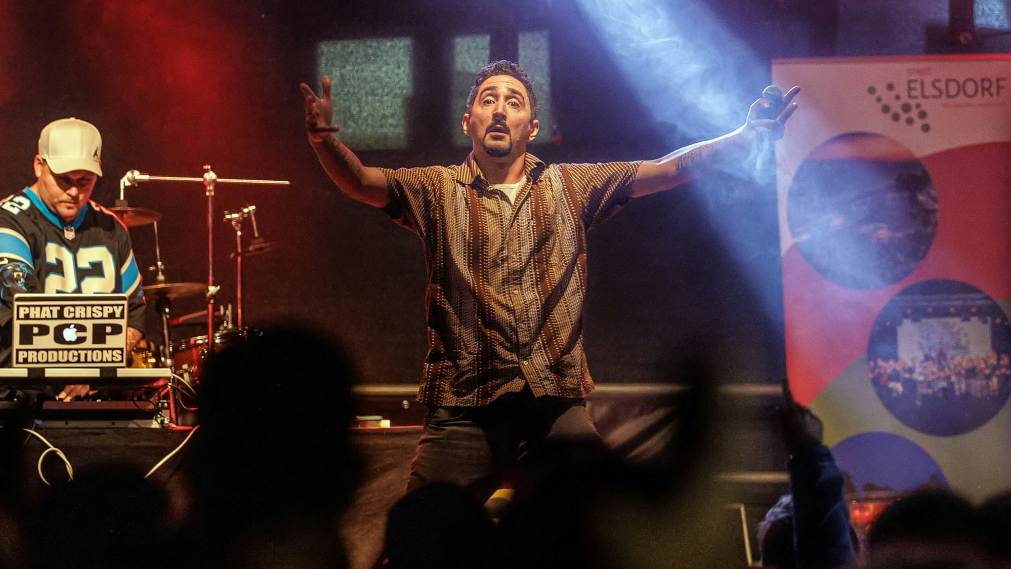 Sänger Eko Fresh singt mit ausladender Geste auf einer Bühne und wird von Scheinwerfern angestrahlt.