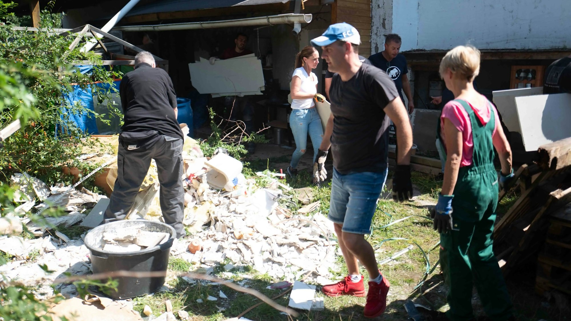 Ein Schutthaufen liegt mitten im Garten. Helfer gehen emsig ihren Arbeiten nach.