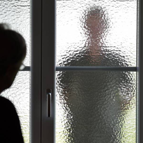 Eine Frau steht an einer Glasscheibe, hinter der ein Stalker steht. (gestellte Szene).